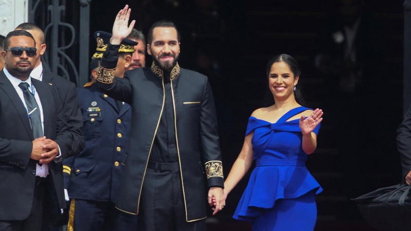 El presidente de El Salvador, Nayib Bukele, saluda a la audiencia junto a su esposa, Gabriela de Bukele, en la ceremonia de su segundo mandato. 